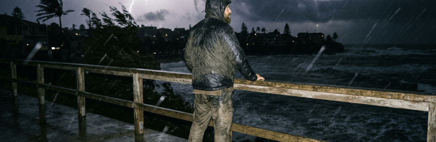 Man standing on wet pier looking at lightning over stormy ocean