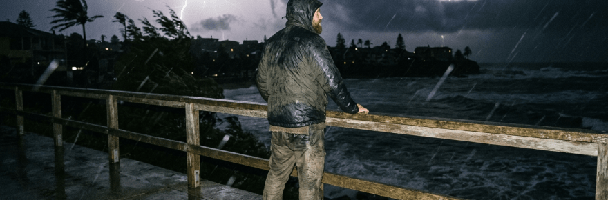 Man standing on wet pier looking at lightning over stormy ocean