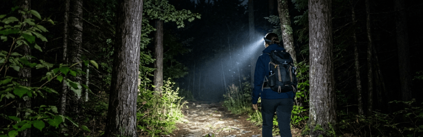 Hiker wearing backpack and headlamp walking on a rocky forest trail at night
