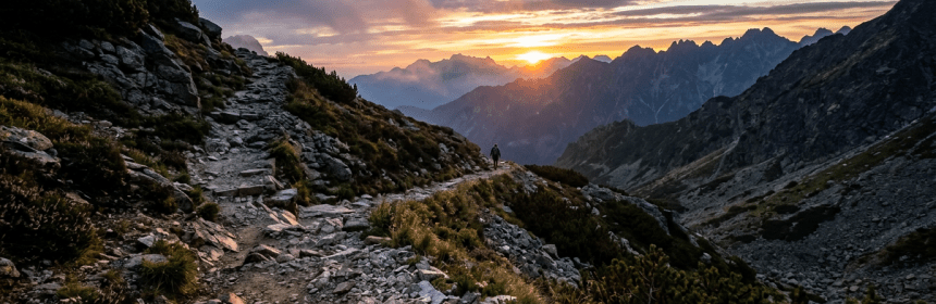 Hiker walking on rocky mountain trail with sunset and peaks in background