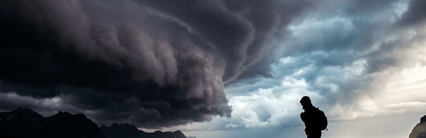 Silhouette of a person standing on rocky shore with stormy sea and dramatic dark clouds overhead