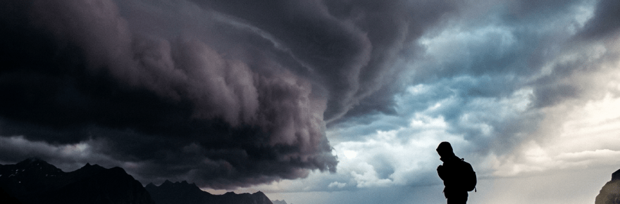 Silhouette of a person standing on rocky shore with stormy sea and dramatic dark clouds overhead